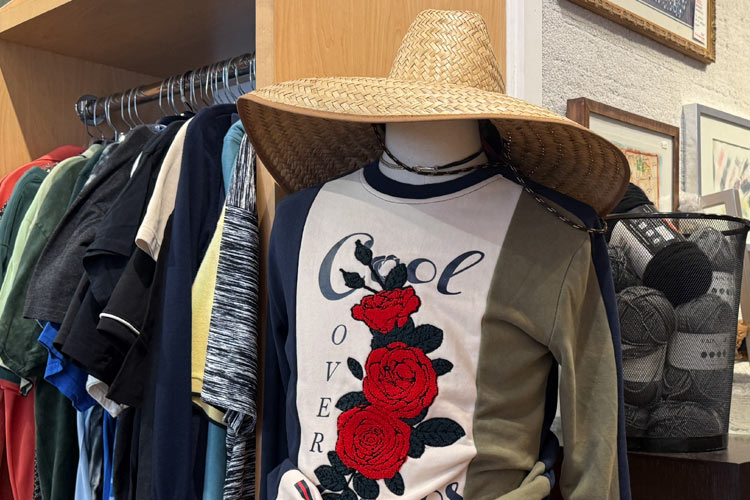 Mannequin wearing a rose-print shirt and straw hat beside a rack of men’s clothing.
