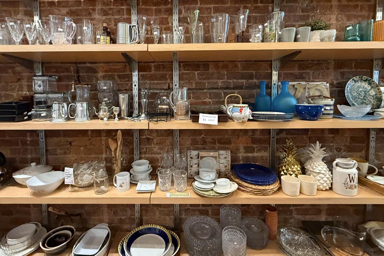 Shelves of secondhand glassware, dishes, mugs, bowls, and decorative housewares at the Park Slope thrift shop.